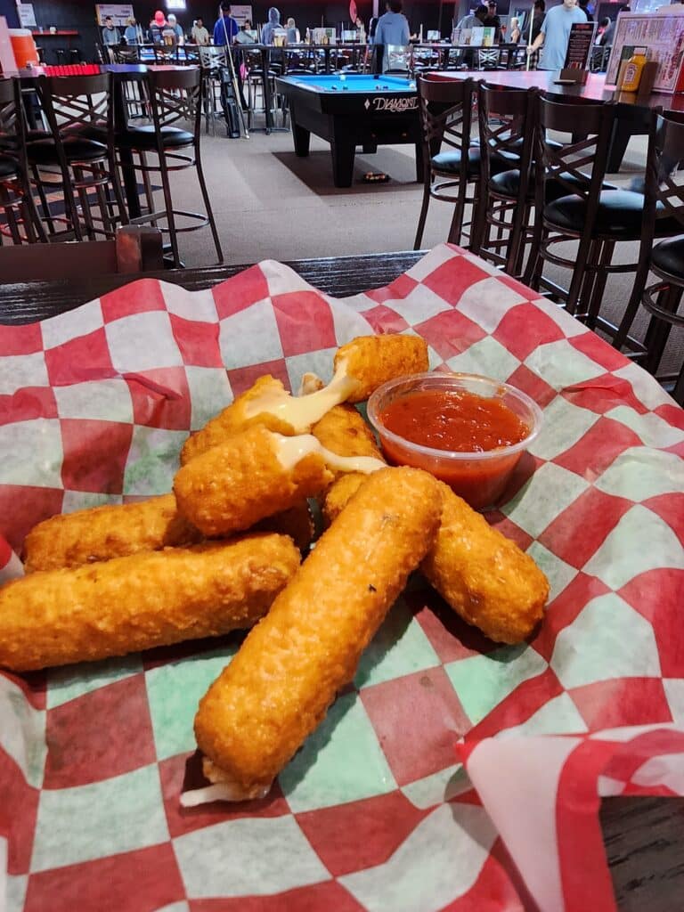 Golden fried cheese sticks oozing mozzarella, paired with marinara sauce at Jimmy’s Pro Billiards, with pool tables in the background