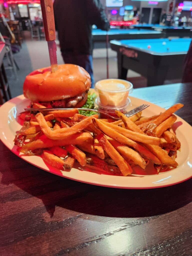 Juicy grilled cheeseburger with lettuce on a toasted bun, served with crispy hand-cut fries and dipping sauce at Jimmy’s Pro Billiards