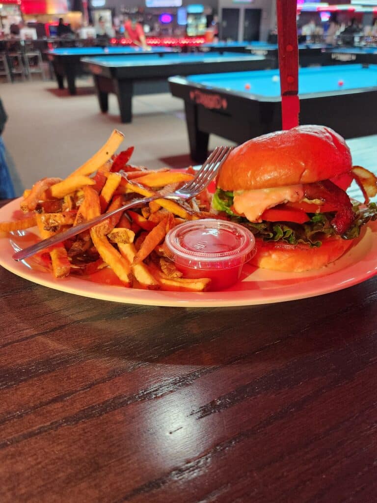 Grilled Chicken Sandwich on a brioche bun with lettuce and tomato with house-cut fries and dipping sauce, served in Jimmy’s Pro Billiards pool hall atmosphere