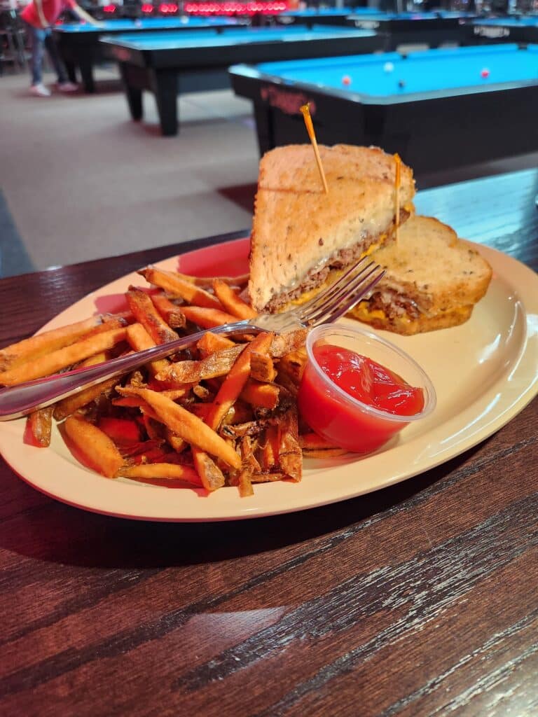 Hearty patty melt on grilled sourdough bread with cheddar and onions, served with crispy hand-cut fries and ketchup at Jimmy’s Pro Billiards